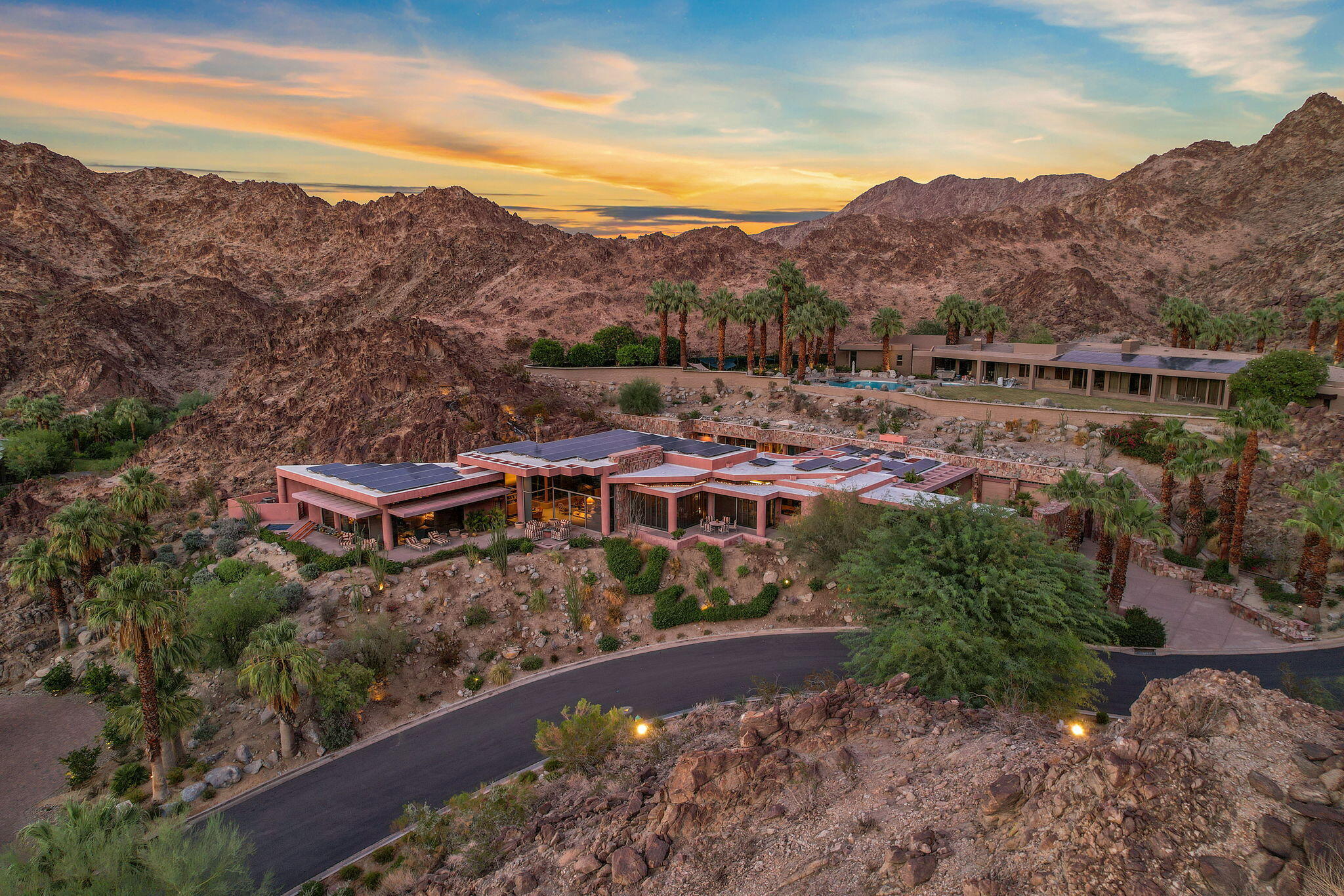 This contemporary compound within the gates of the renowned Vintage Club features scale and volume rarely found. Embedded into the natural mountain terrain, floor to ceiling windows and doors boast expansive views of the desert below. Situated on a 52,836 square foot lot, the 7,258 square foot layout offers a seductive and spacious silhouette with a natural flow into oversized living spaces including, a sunken living room with fireplace, a formal dining area, and a gourmet chef's kitchen, all complemented by windows showcasing the dramatic backdrop. Four ensuite bedrooms, including a primary suite with picturesque vistas, surround the pool offering a seamless transition of indoor-outdoor living that only the desert can provide. Two guest suites share a common sitting area and kitchenette with a private entry. An owned solar grid minimizes maintenance costs. The prime location and unique infrastructure poses an opportunity for customization and personal touch.