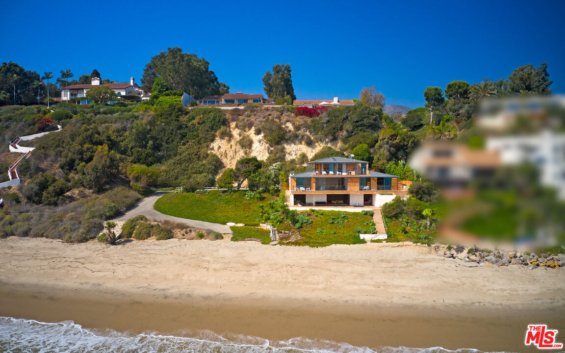 Located in a gated community on a private road, this modern estate designed by architect William Hefner embraces the Malibu lifestyle from the moment you arrive! With 88 feet of beach frontage, its envious location is steps from the beach and boasts 180 views of the ocean from the expansive deck. As you enter through the pivot glass door into the stone foyer with interiors designed by Billy Cotton, the spacious living room draws you in to capture the views as you relax in front of the fireplace. The sliding glass doors open to the expansive deck to enjoy indoor-outdoor living. Experience a one-of-a-kind kitchen equipped with Miele and Gaggenau appliances, floating shelves, a built-in keg, wine fridges, and a large walk-in pantry. With skylights overhead, an ocean view breakfast nook and additional island bar seating, sliding glass doors open to a BBQ island, and an outdoor dining area. The owner's suite is a masterpiece spanning the entire top floor for the ultimate privacy. Wood floors and glass walls provide a remarkable backdrop to display your art collection on the built-in shelving throughout the room. The owner's ensuite boasts uncompromising quality with a Toto washlet, freestanding tub, resort-style shower, and stone countertops. The suite is complete with a large walk-in closet and a wrap-around balcony. Two additional bedrooms and a media room round out the spaces in this estate. The media room features wood-paneled walls and doors leading to the deck, complete with a lounge area, jacuzzi, additional dining spaces, and heaters, providing everything you need for year-round entertaining. A meticulously landscaped yard with low-maintenance succulents provides year-round beauty to enhance the outdoor spaces. In addition, to a two-car garage, guest park area, and gated entry, the home is equipped with security cameras on the property, a full-house alarm system, and a built-in sound system. This Malibu estate is beautifully appointed with attention to detail and offers exquisite living for the discerning buyer. Schedule your private tour today.