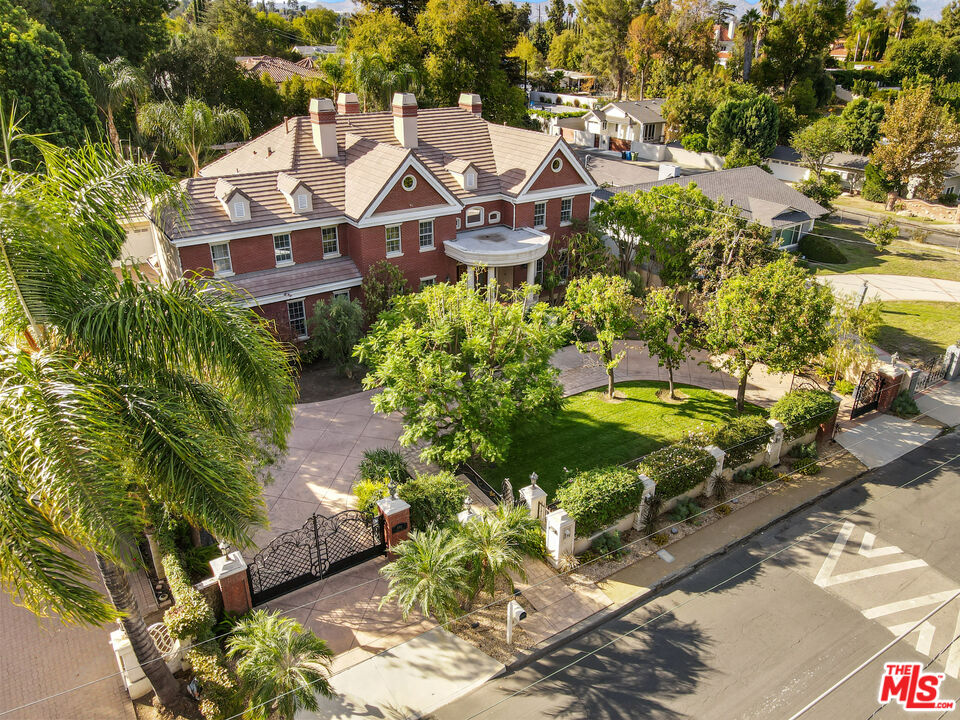 This stunning Colonial-inspired home, sits on a tree-lined street in highly desirable Tarzana, south of the boulevard. Situated on a 20,000-square-foot flat parcel, this gated property has approximately 100' of frontage. Enter through beautiful oversized front doors to find soaring ceilings, a wonderfully traditional floor plan with a formal living room, dining room, wood-paneled office, and an elegant staircase ascending to 3 en-suite bedrooms, an office, and a media room or the elevator for easy access. The spacious primary bedroom is an oasis unto itself with a seating area, fireplace, and plenty of light. Also, the oversized closet and spacious bathroom are an added bonus. Here you will find an open-concept kitchen and family room, that flows seamlessly out to the patio and sunny backyard with a gorgeous swimming pool, the perfect place for friends and family to gather. There are 2, two-car garages - one is being used as an art studio. This is the first time the home has been on the market in 18 years and is a true sanctuary from the bustle of the city.