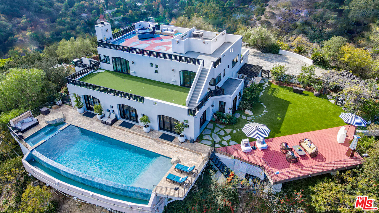 13211 Mulholland Dr Beverly Hills, California Seeking the ultimate Beverly Hills sanctuary where you can leave behind the hustle and bustle of everyday life? Look no further than this beautifully crafted secluded estate that provides the perfect blend of luxury and tranquility while being just moments from everything LA has to offer! Enviably set on over an acre atop famed Mulholland Drive, this residence commands spectacular views from an impressive 1,300 ft above sea level. A gated, private driveway leads to the grand 2-story facade. Inside, new luxury flooring and dark wood trim tastefully contrasts crisp white tones. Graceful archways greet you in the generously sized open entertainment areas as you seamlessly transition from one room to another. Multiple French doors in the family room and dining area frame sweeping panoramas of the city, ocean, and Catalina Island. A raised-hearth fireplace with a stacked-stone surround anchors the stylish volume ceilings, warming the living room as you gather. Shake up your favorite cocktails and head outside to relax by the infinity pool and appreciate the stunning views in absolutely every direction you look. Sleek and sophisticated, the chef's kitchen equips you with top-notch stainless steel appliances, abundant white wood cabinetry, granite countertops, an oversized island, and a breakfast nook with access to the patio. Working from home is even better in your private office overlooking breathtaking views. Admire picturesque sunsets from your well-sized bedrooms, adorned with mirrored closets and French doors that open to the large wraparound balcony. Surpassing all in size, the primary suite has a walk-in closet and an ensuite with a spa-like soaking tub and scenic views. Endless hours of fun and leisure await in your expansive outdoors that offers numerous entertaining decks, a resort-style infinity pool, two putting greens, and a pool cabana. Alfresco dining is bliss under the pergola as you enjoy delicious meals prepared on the built-in BBQ island. On cooler nights, sip a refreshing nightcap as you take a soothing dip in the rooftop spa while watching the sunset views and city lights twinkle below. Other notable features include a large private vineyard, a koi pond in the zen garden, a waterfall, and a professional music studio. The estate vineyard produces private reserve wines with multiple varietals, including Pinot Noir, Sauvignon Blanc and Cabernet. The golf decks are beautifully manicured with 9 holes and white artificial sandpits. Convenience is yours with smart-home technology including a Control4 music system, two Nest-operated HVAC units, app-controlled landscape lighting, home protection system, wireless pool features and a 16-camera CCTV system. Its fabulous location puts you near the world-class shopping, dining, and attractions of the Sunset Strip, West Hollywood, and Beverly Hills. Come grab the rare chance to call this Mulholland Oasis home!