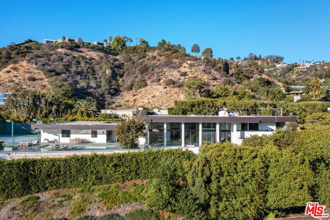 1120 Wallace Rdg Beverly Hills, California Award-winning Prime Trousdale designed by master architect Edward Fickett, FAIA. This tennis court estate, with grandfathered in night lights that can never be done again in Trousdale, features privacy, volume, and resort-like amenities. Tucked behind gates, this impressive residence is situated on a jumbo lot, boasts architectural pedigree, floor-to-ceiling windows, and A+ views of the city and Pacific Ocean. Home is move-in ready, but the historical tag has been removed which allows for major renovations to be done if desired. A buyer can choose to move forward with the approved plans to expand on the historical nature of the property, which already include 18' ceilings and dramatic roof elevation change, or keep it in its current state. Double door entry reveals an open and versatile floor plan showcasing a light-and-bright formal living room, an indoor living tree and an elevated dining room. A spacious upstairs primary suite has it all; a loft area, dual bathrooms, walk-in closets, and a terrace with breathtaking views. The sun drenched, dine-in, gourmet kitchen was renovated with a bold, yet classic palette and finished with a large island counter, breakfast bar, and fine appliances. A sitting room features an entertainer's bar, a double-sided fireplace, treetop views and access to a flat grassy outdoor pad. The home's exterior offers an inviting backyard with pool and large patio, a full-size and flood-lit n/s tennis court, fire pit, and a generous space for a gathering. Close to all that Beverly Hills has to offer, this offering is not to be missed.