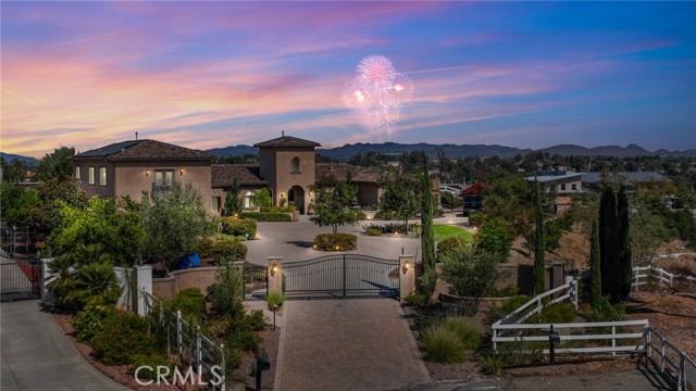 Indulge your desire to live in the Italian wine countryside without ever having to leave Southern California! This incredible Tuscan-inspired estate was custom built in 2015, sitting on 5.72 acres of land complete with your own personal vineyard. As you pull up to the property, you are welcomed by a private iron gate, through which you'll encounter the paver-stoned driveway and motor court. With dark, hand-scraped hardwood floors, crown molding, and plantation shutters throughout, this largely single story home exudes elegance. The sunken formal living room is immediately through the entrance, with a gorgeous fireplace and views of the grounds. Just to your left is the formal dining room, with a stunning coffered ceiling, built in serving buffet, and French doors to the backyard. Continuing down the hallway, there is a bathroom situated just off the backyard, complete with a shower for poolgoers. Your dedicated wine storage room is on the left, with an iron grapevine door. An informal dining area is situated right off the great room, with its built in entertainment center, picture window, further backyard access through a sliding door, and open to the incredible chef's kitchen! This gourmet kitchen has tile flooring, stainless steel Viking appliances (built in fridge, double oven, six burner range, and microwave) and Bosch dishwasher; travertine tile backspash, a pot filler, glass-doored pantry, and an enormous island offering ample storage space and a second sink. Off the kitchen is the guest wing of the home, with a sizable laundry room, gym, two downstairs guest bedrooms (both with en suite bathrooms), access to the three car garage, and above the garage is a private guest suite, with its own living room, bathroom, bedroom, and incredible views of the grounds. On the opposite side of the house is the owner's wing, which has an office with a fireplace and the primary suite - a bathroom with his and her sinks, a makeup counter, a spa tub, and a walk in shower; a walk-in closet with extensive built-in storage and an island folding table; and the bedroom with its own fireplace and sliding doors to the backyard. In the backyard is a kitchen, complete with combo ice chest/sink, fridge, high heat stove, BBQ, and bar seating. Pool with spa and Baja reef. Sport court; putting and chipping green; playground; sunken fire pit... truly an entertainer's dream. 22 OWNED solar panels, 20+ fruit trees, and the crown jewel - a 1400 vine vineyard of Syrah grapes.