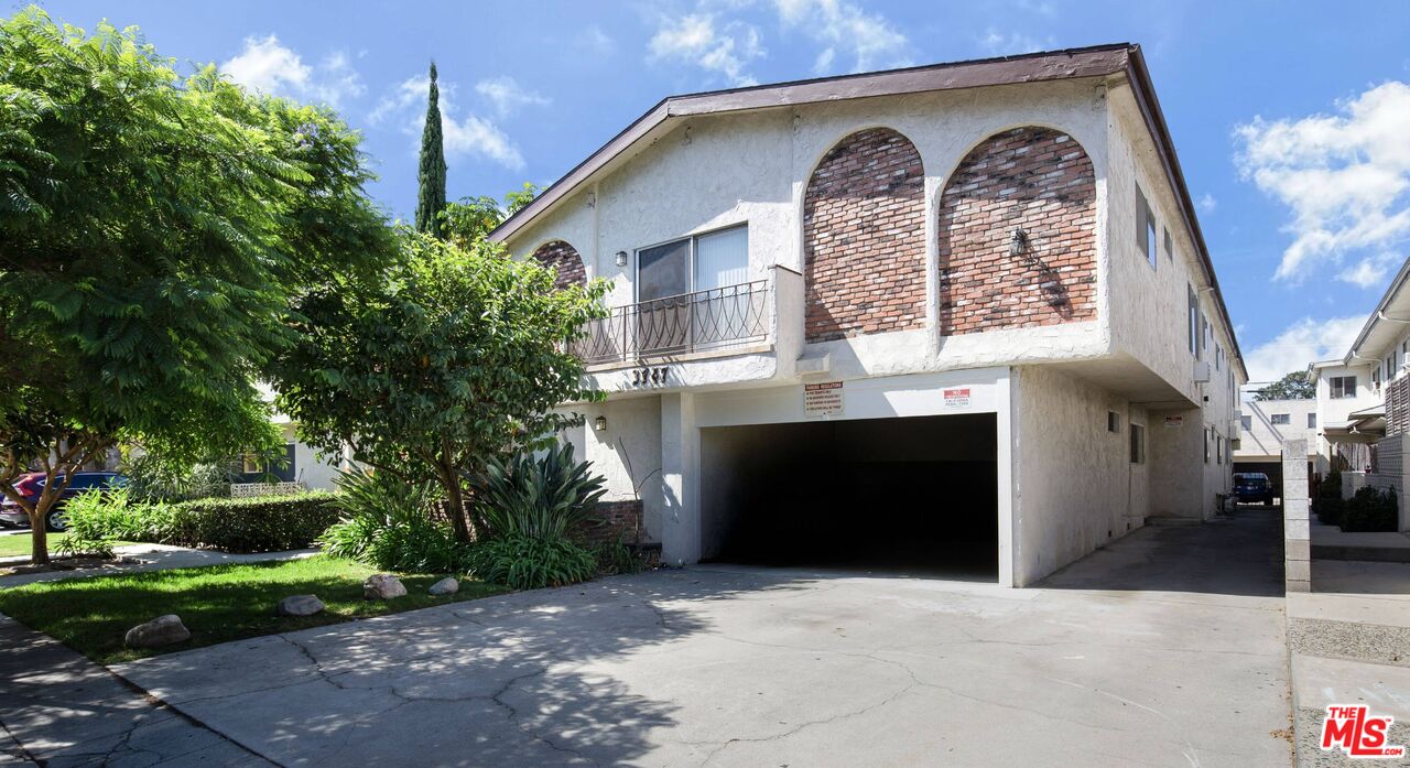 Two-story stucco residential building with brick arches, a balcony, and a wide carport.