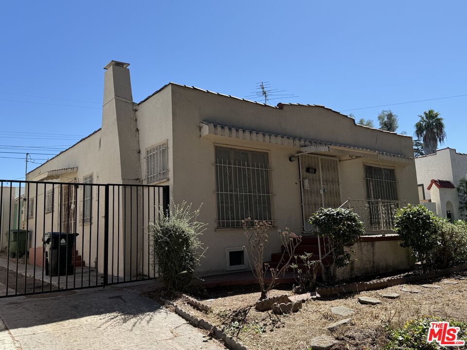 Single-story stucco house with barred windows, a black metal gate, and sparse front landscaping.
